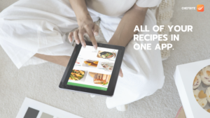 A lady holding a tablet on the floor of a kitchen and the tablet has Chefbite app open and she is scrolling through food recipes
